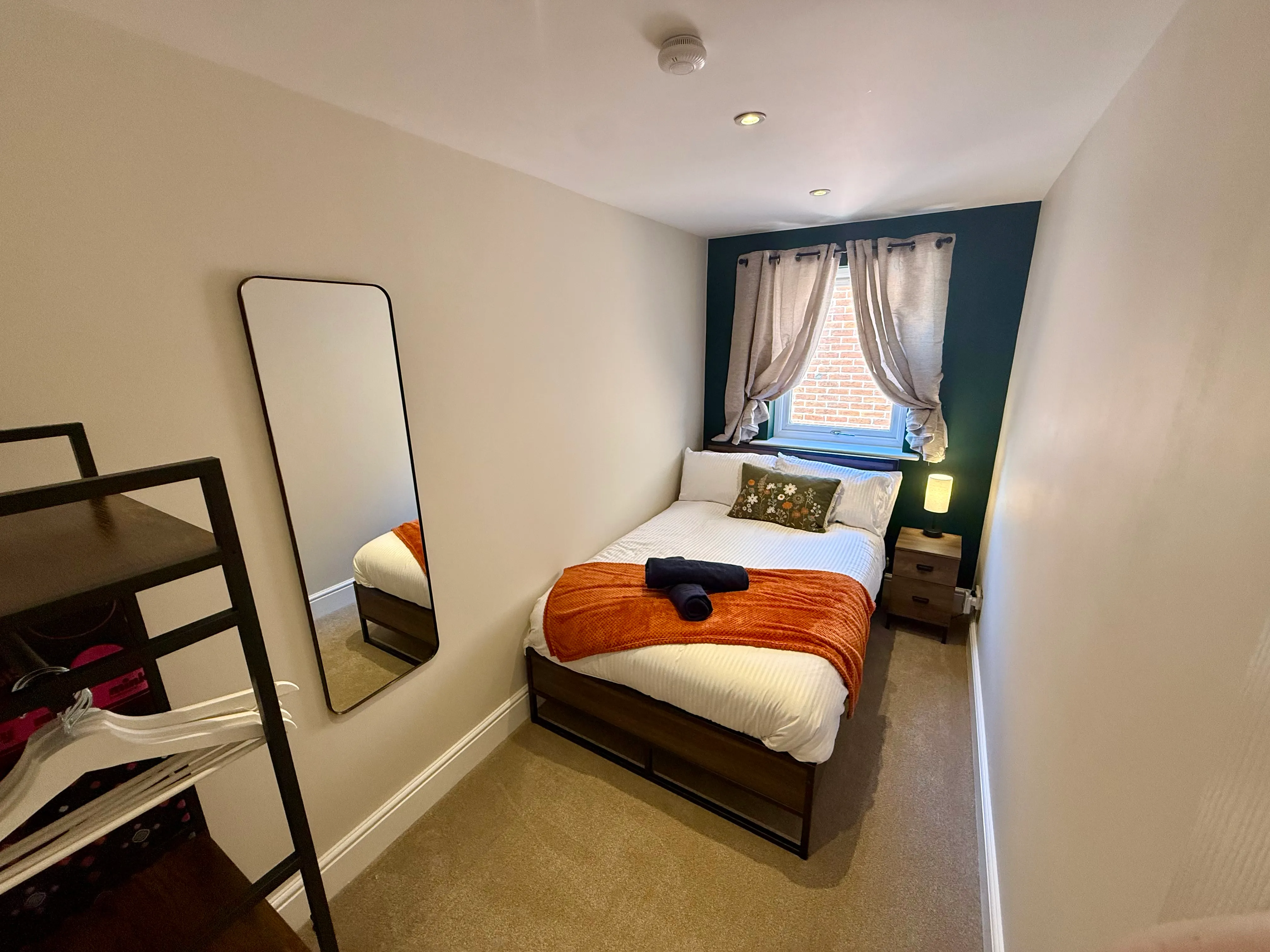 The small double bedroom with a teal accent wall and orange throw