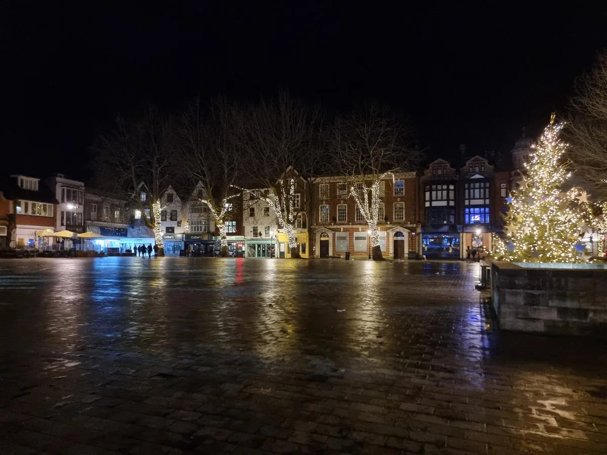Market Place in Salisbury at night at Christmas, with fairy lights on the trees reflected in the wet paving